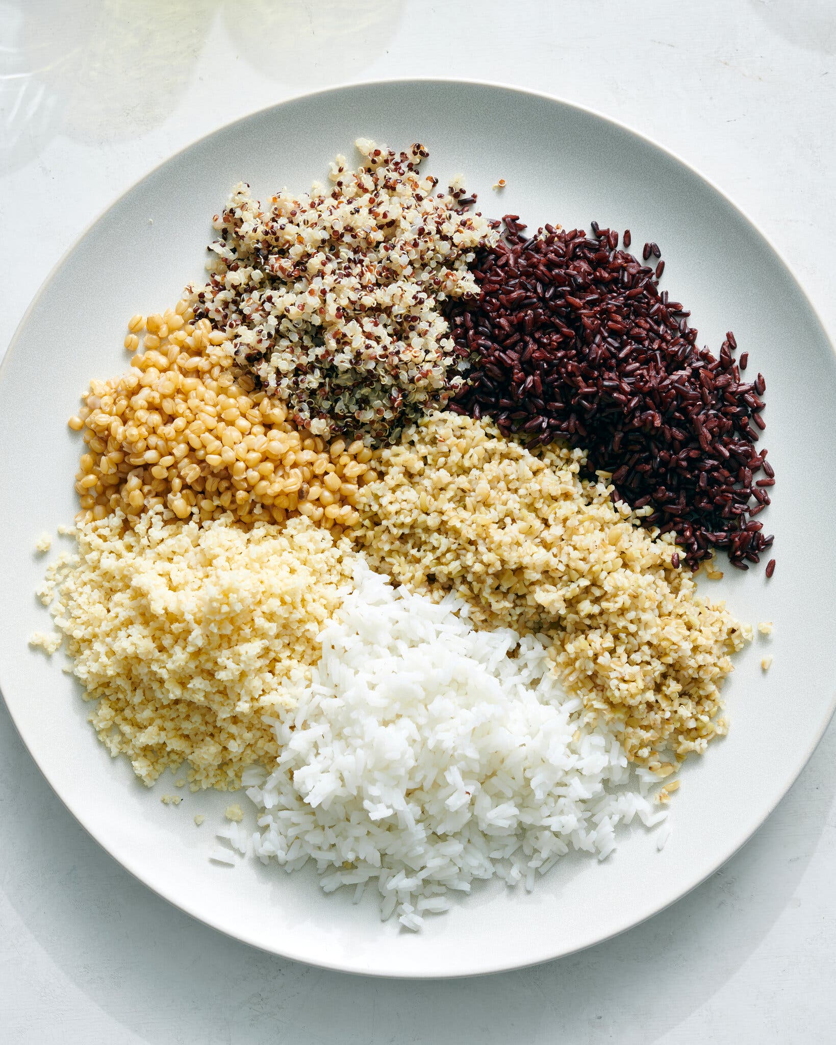 A white plate holds small mounds of six different grain varieties.