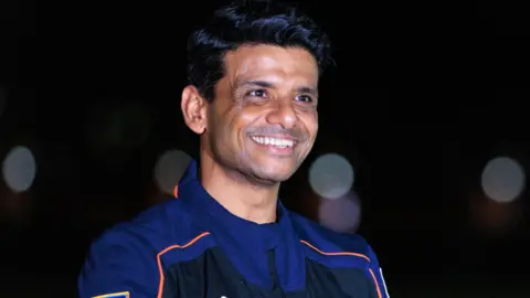 EPA ISRO (Indian Space Research Organisation) astronaut Shubhanshu Shukla, one of the four members of Axiom Mission 4, is pictured here with a wide smile, in a dark backdrop.