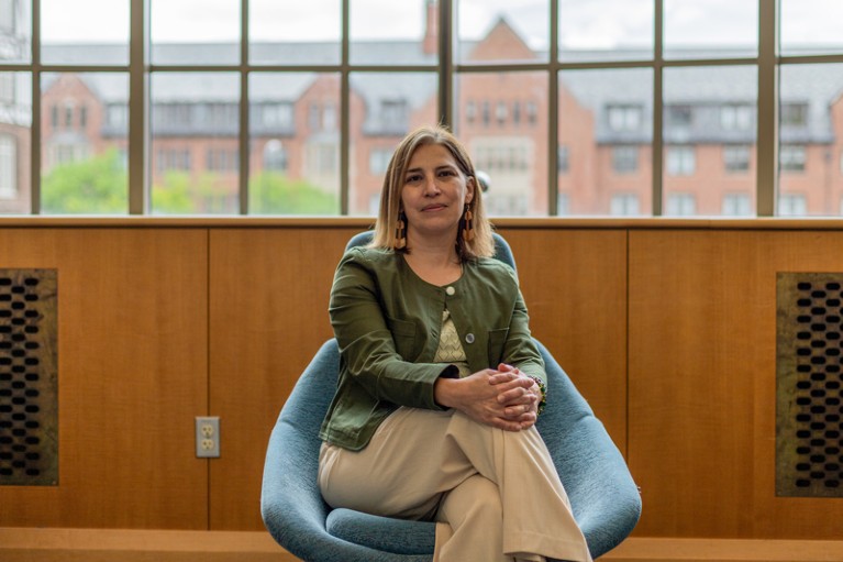 Portrait of Briana Mezuk sitting in a blue chair in front of a large window