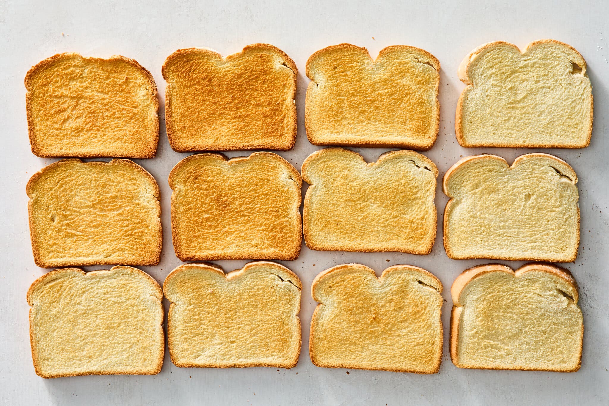 An overhead image of 12 slices of bread with various degrees of toasting.