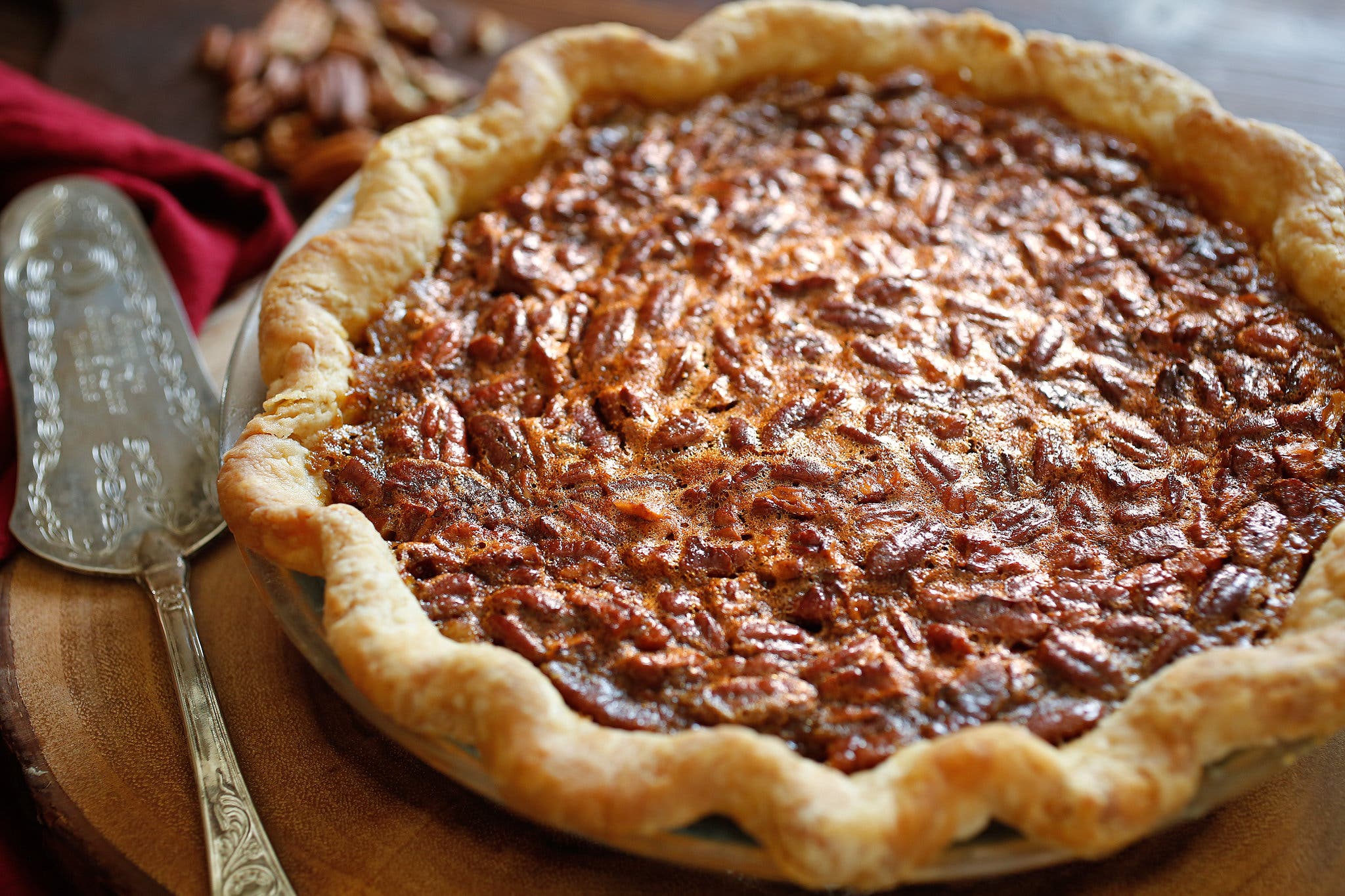 A pecan pie, sitting next to a cake server and on top of a wooden cutting board.