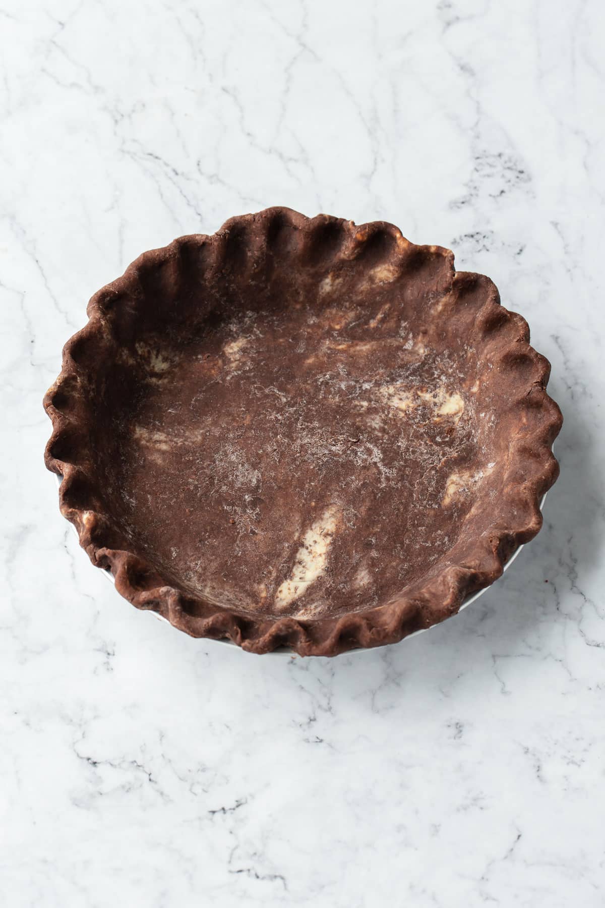 Unbaked chocolate pie crust with fluted edges on a marble background.