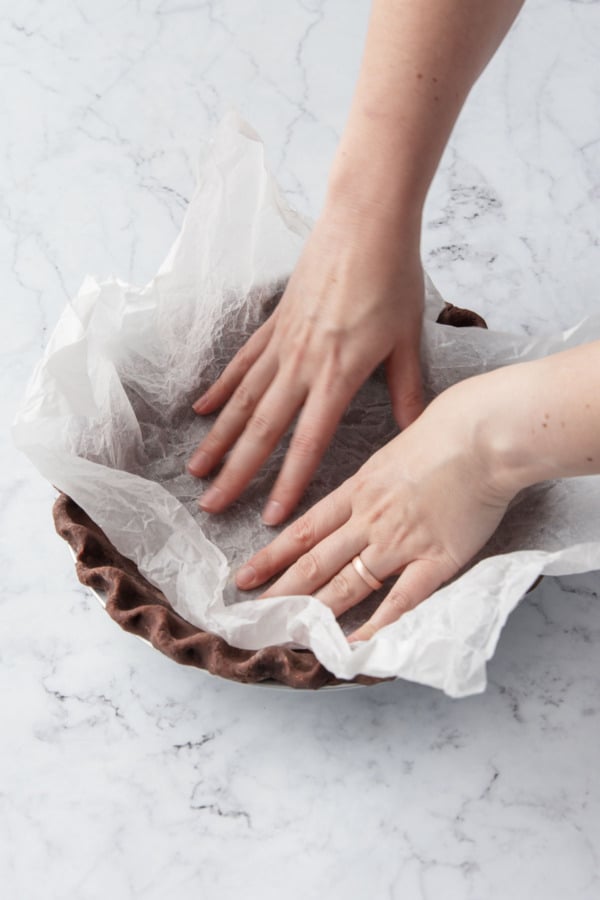 Lining the chilled, fluted crust with crinkled parchment paper.