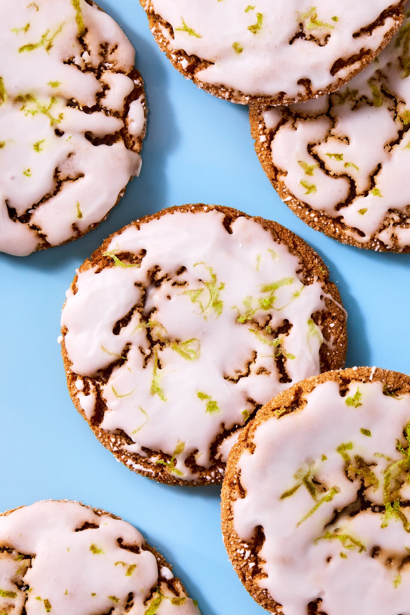 An overhead image of a half-dozen ginger cookies topped with icing and lime zest.