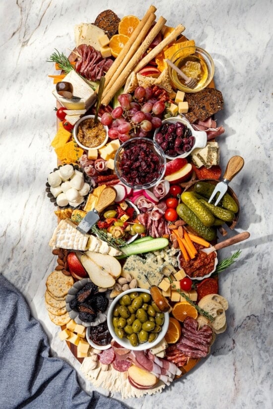 Large charcuterie and cheese board with fruit, pickles, olives, and spreads.