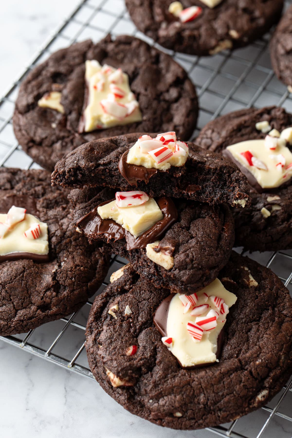 Chocolate Peppermint Bark Cookies on a wire cooling rack, one cookie broken in half to show the inside texture and melty chocolate peppermint bark on top.