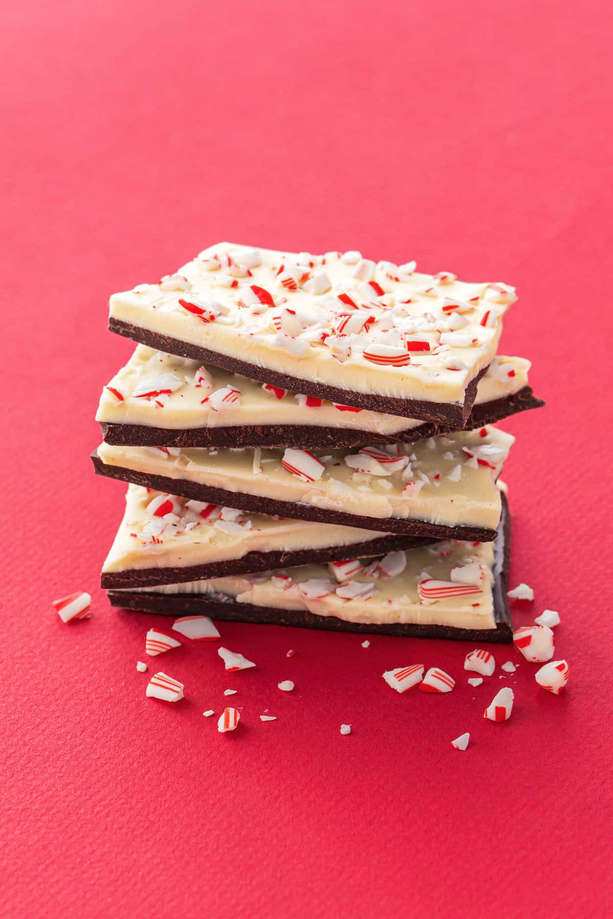 Stack of rough broken pieces of peppermint bark on a red background with candy cane crumbs.
