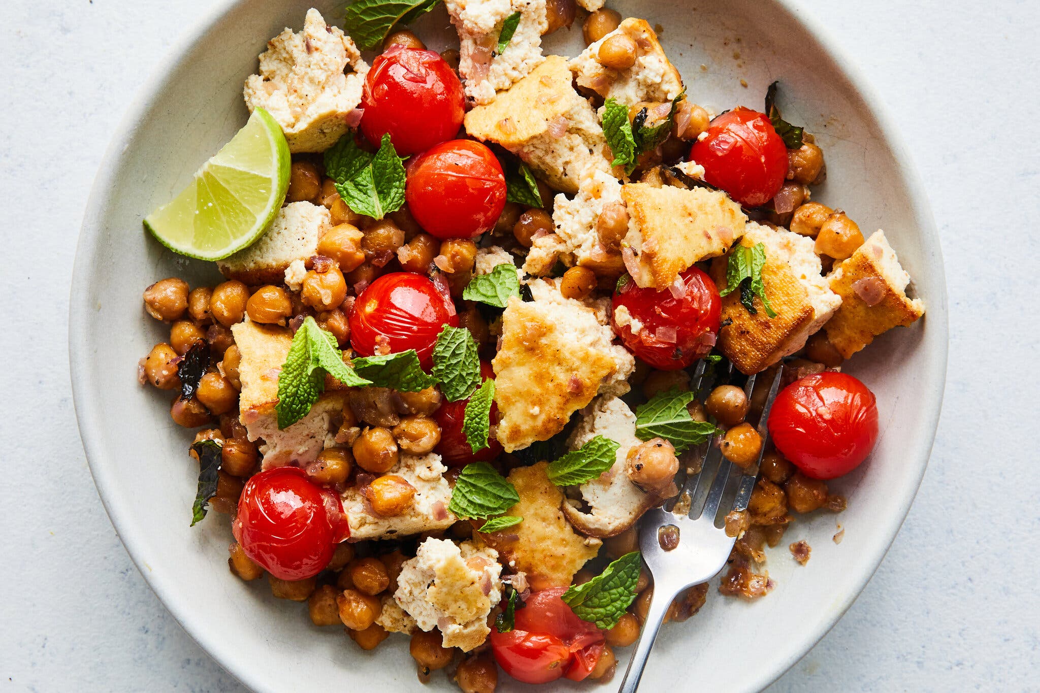 An overhead image of chickpeas and torn tofu topped with tomatoes and herbs.