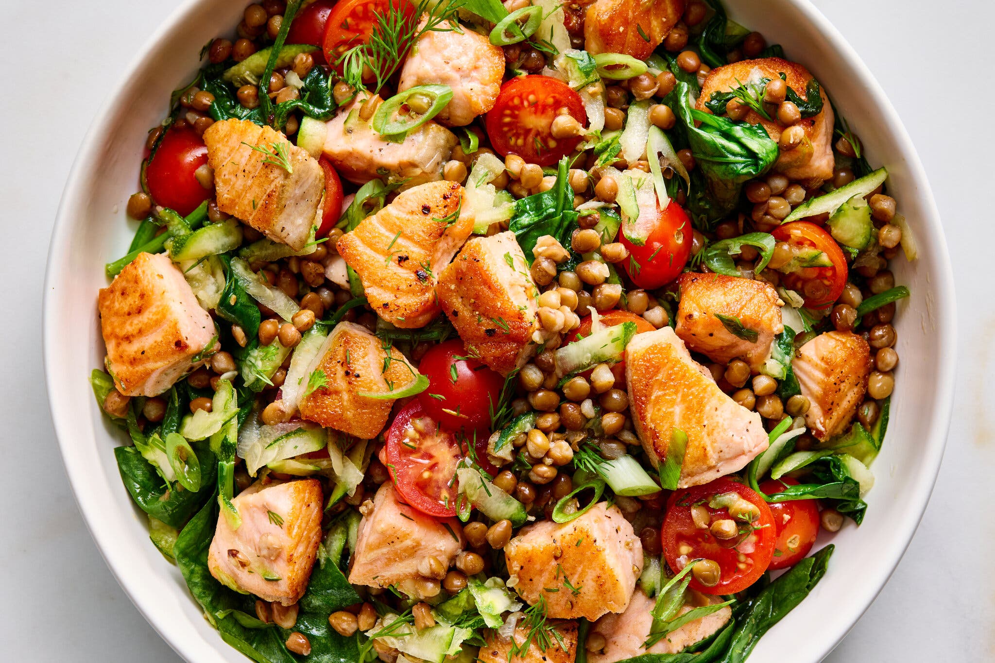 An overhead image of salmon chunks in a pot with lentils and spinach.