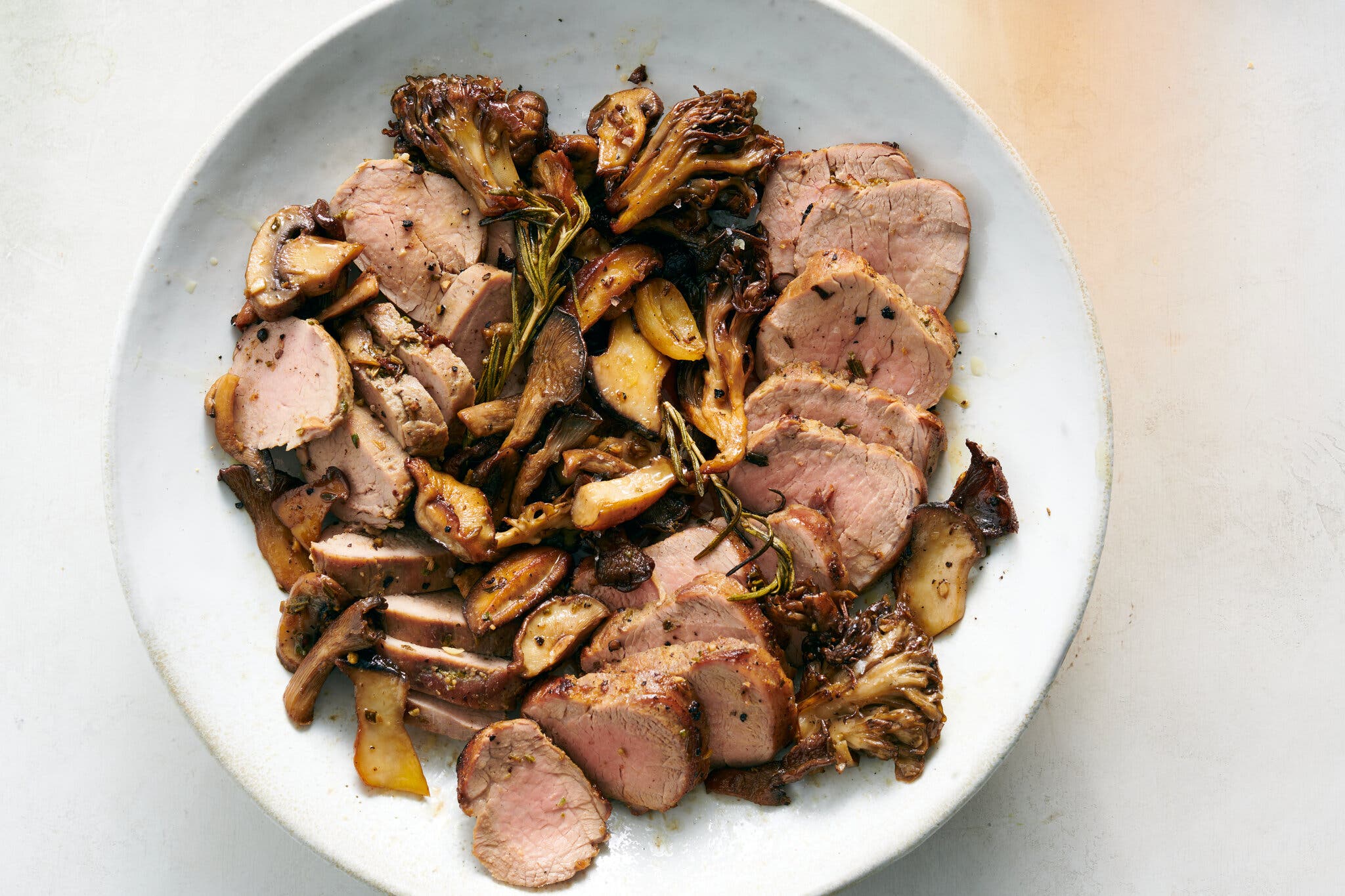 An overhead image of sliced pork tenderloin with mushrooms and herbs.