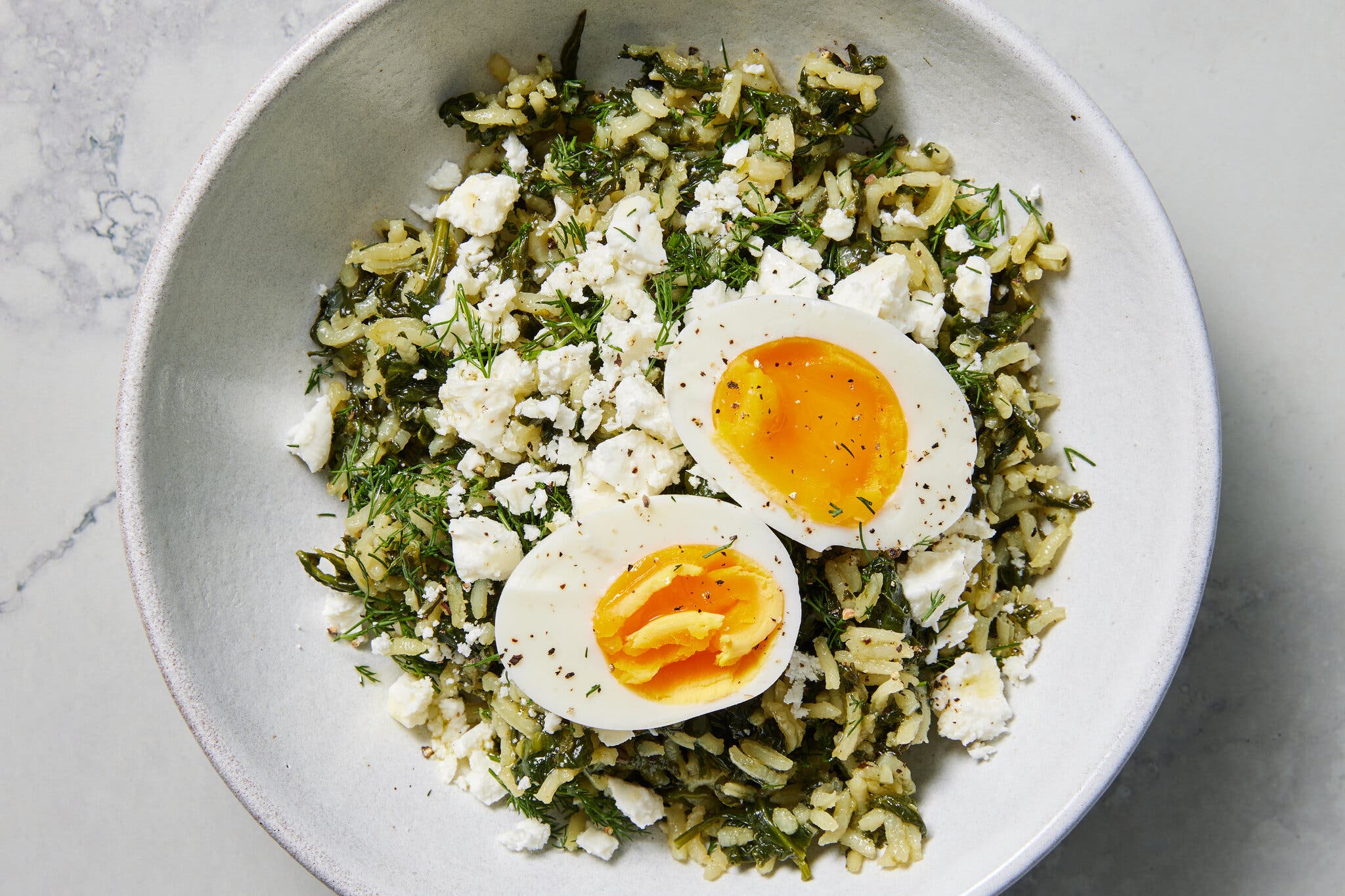 An overhead image of a bowl filled with rice, herbs and spinach and topped with jammy eggs.