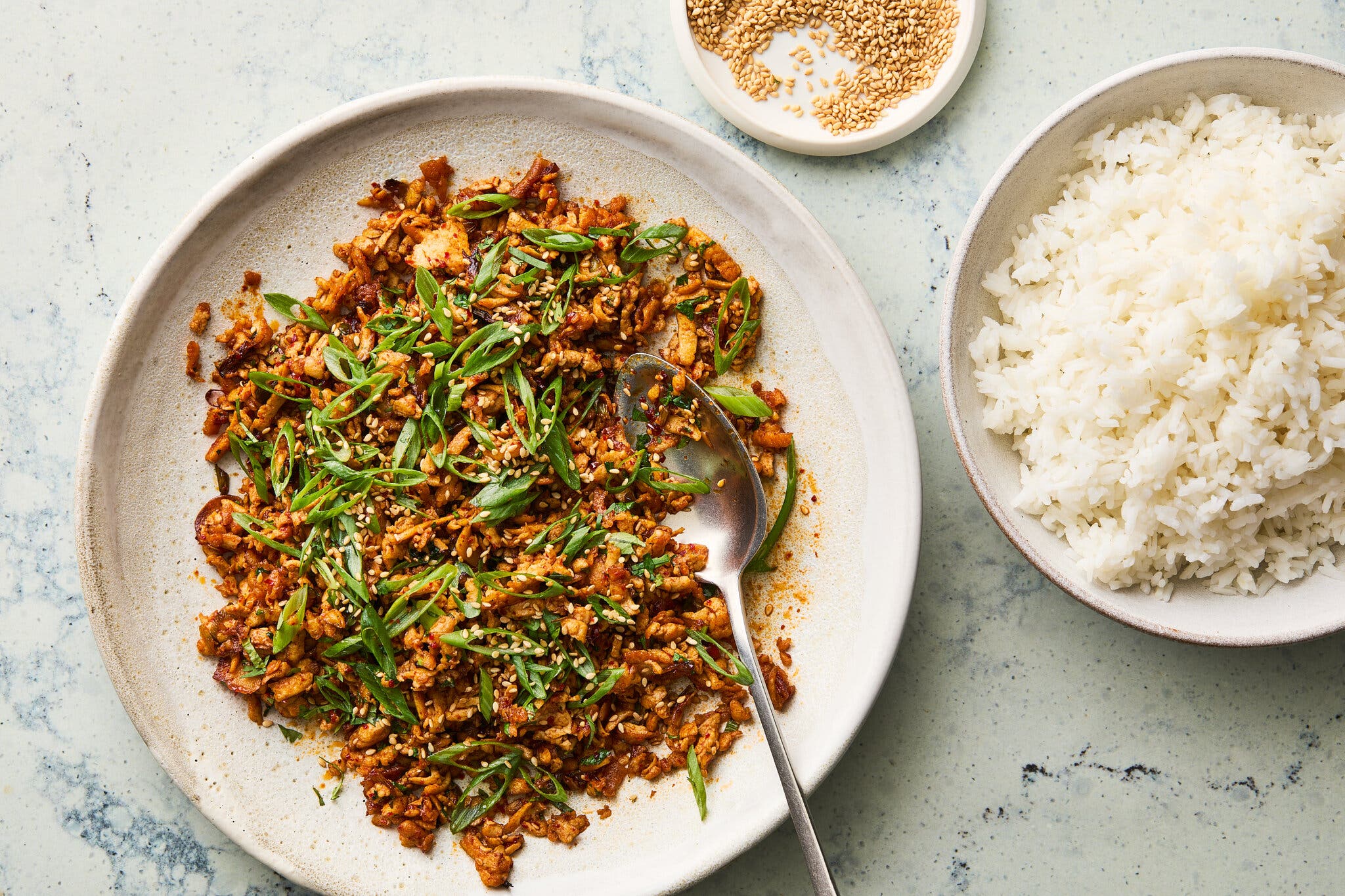An overhead image of grated tofu on a plate next to a bowl of rice.