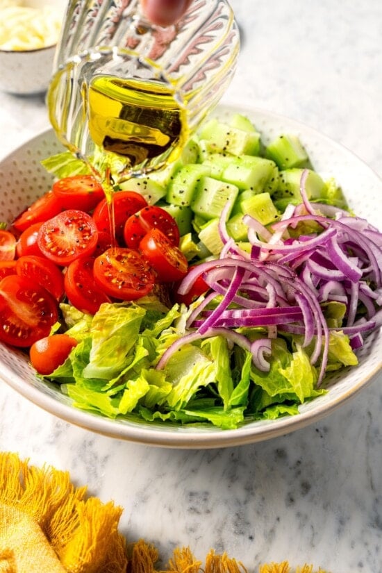 Pouring olive oil over vegetables for Italian chopped salad.