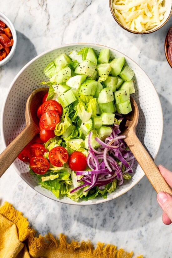 Two spoons tossing Italian chopped salad in bowl.
